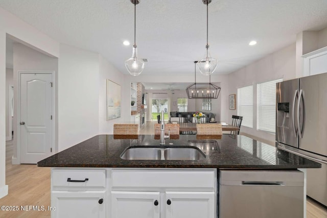 kitchen featuring appliances with stainless steel finishes, light wood finished floors, decorative light fixtures, a center island with sink, and white cabinetry