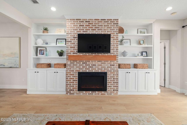 unfurnished living room featuring built in shelves, a brick fireplace, and light wood-style floors