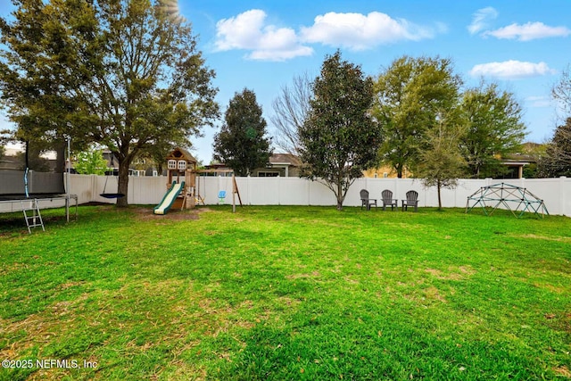 view of yard with a trampoline, a fenced backyard, and a playground