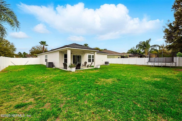 back of house featuring a fenced backyard, a trampoline, a patio area, a yard, and stucco siding