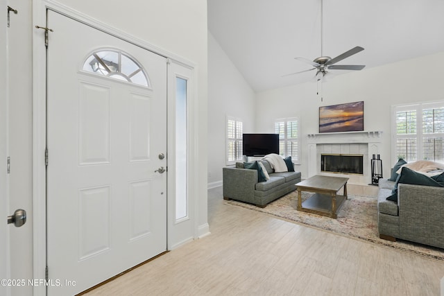 entryway with a wealth of natural light, a tile fireplace, high vaulted ceiling, and a ceiling fan