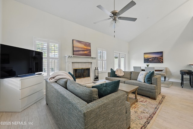 living area featuring high vaulted ceiling, ceiling fan, light wood finished floors, and a tiled fireplace