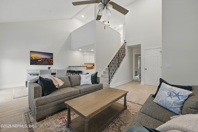 living room with high vaulted ceiling, light wood-style floors, stairs, and baseboards