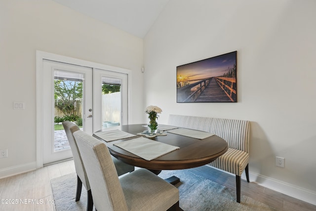 dining space featuring light wood-style flooring, lofted ceiling, baseboards, and french doors