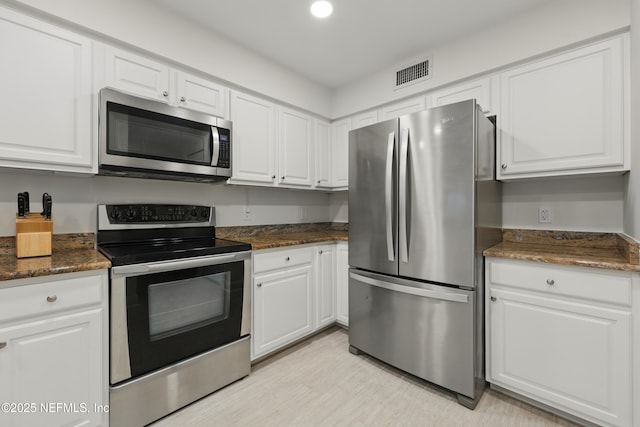 kitchen featuring white cabinets, visible vents, stainless steel appliances, and dark stone countertops
