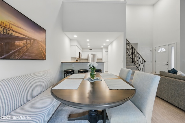 dining area featuring recessed lighting, a high ceiling, light wood-style floors, and stairs