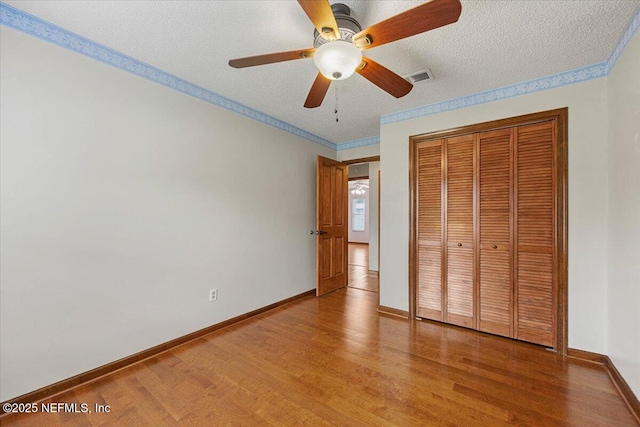 unfurnished bedroom with crown molding, visible vents, light wood finished floors, and a closet