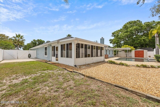 back of house featuring a storage unit, a gate, a chimney, an outdoor structure, and a sunroom