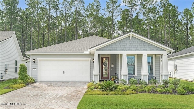 view of front of property featuring roof with shingles, covered porch, a garage, a front yard, and decorative driveway