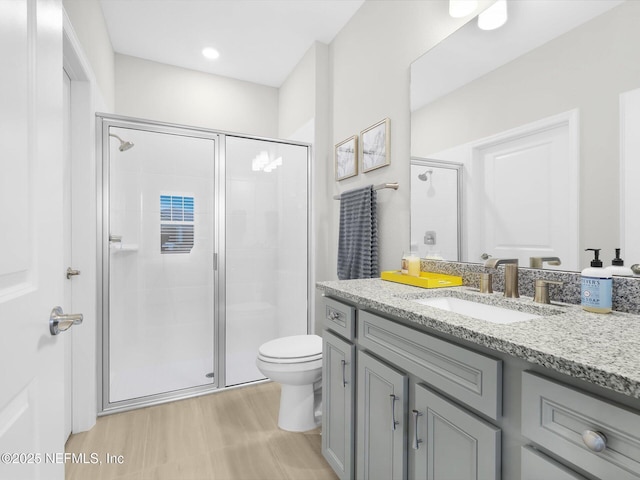 bathroom featuring wood finished floors, vanity, toilet, and a stall shower