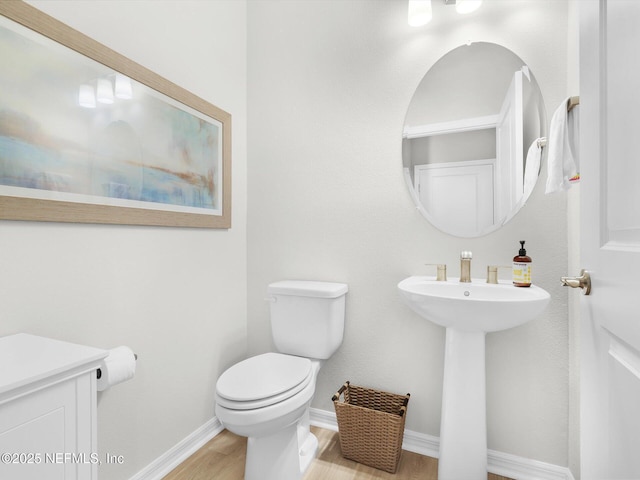 half bath with wood finished floors, toilet, baseboards, and a sink