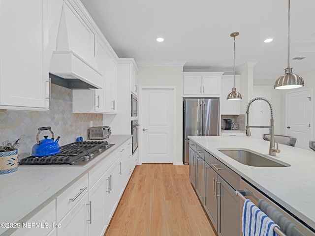 kitchen with a sink, stainless steel appliances, premium range hood, white cabinets, and decorative light fixtures