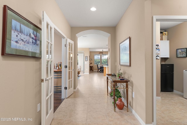 corridor featuring baseboards, arched walkways, light tile patterned flooring, recessed lighting, and french doors