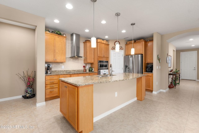kitchen featuring decorative backsplash, appliances with stainless steel finishes, arched walkways, wall chimney exhaust hood, and a kitchen island with sink