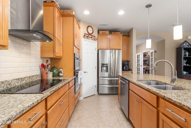 kitchen featuring a sink, stainless steel appliances, decorative backsplash, light stone counters, and wall chimney range hood