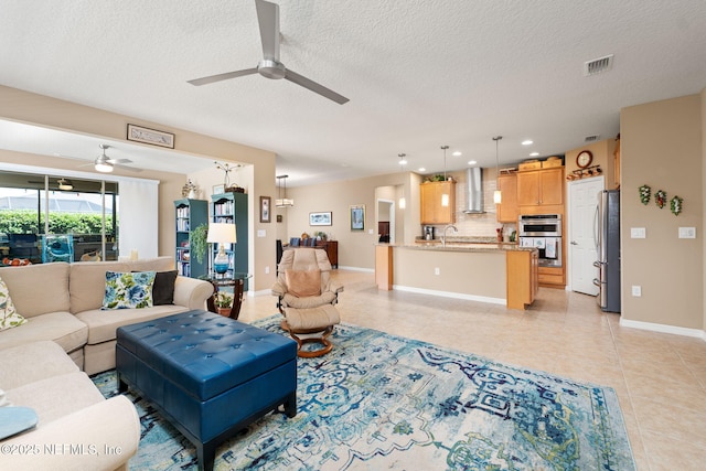 living area featuring light tile patterned floors, a ceiling fan, visible vents, baseboards, and a textured ceiling