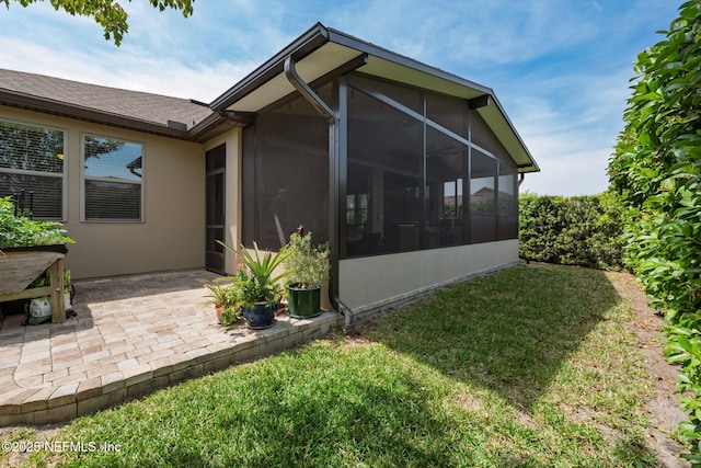 back of house featuring a lawn, stucco siding, a patio, and a sunroom