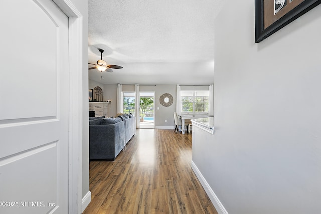 hallway featuring wood finished floors, baseboards, and a textured ceiling