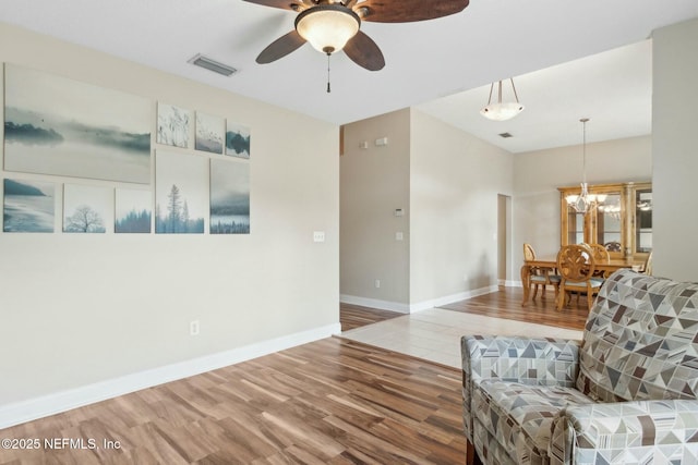 living area with wood finished floors, visible vents, baseboards, and ceiling fan with notable chandelier