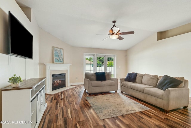 living room featuring dark wood-style floors, a glass covered fireplace, a ceiling fan, vaulted ceiling, and baseboards