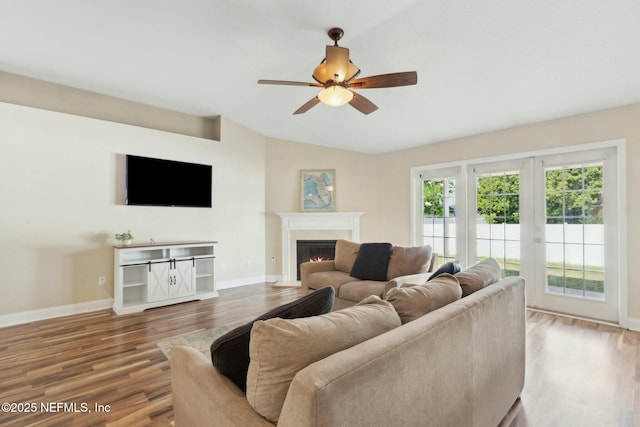 living room with wood finished floors, a ceiling fan, a warm lit fireplace, and baseboards