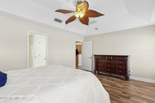 bedroom featuring a raised ceiling, a ceiling fan, visible vents, baseboards, and wood finished floors