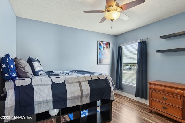 bedroom featuring baseboards, wood finished floors, ceiling fan, and a textured ceiling