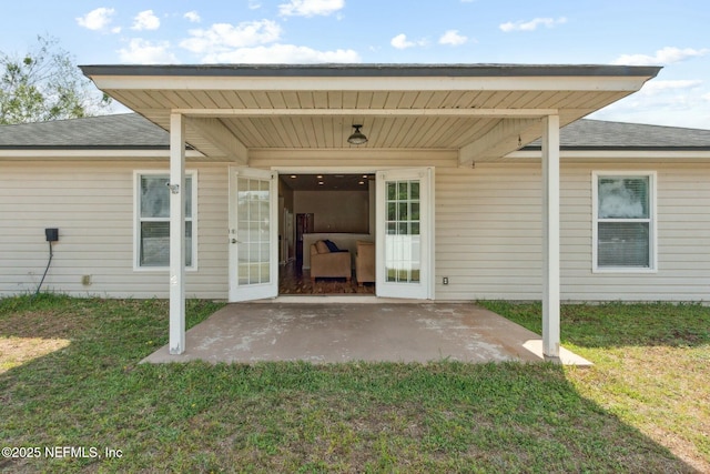 entrance to property featuring roof with shingles, a yard, and a patio