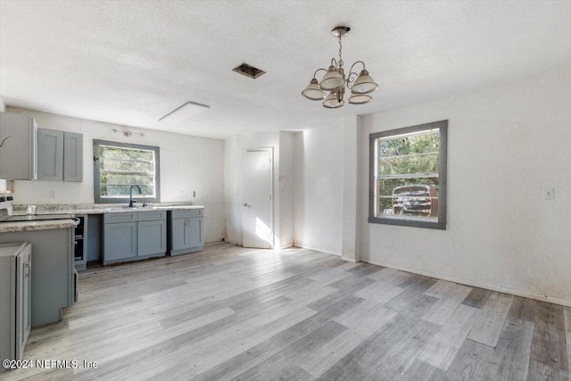 kitchen with visible vents, a sink, light wood-style flooring, a textured ceiling, and a notable chandelier