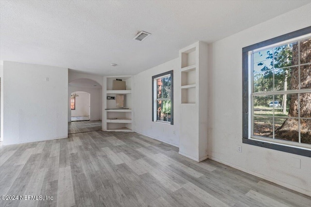 unfurnished living room featuring wood finished floors, a textured ceiling, arched walkways, built in features, and visible vents