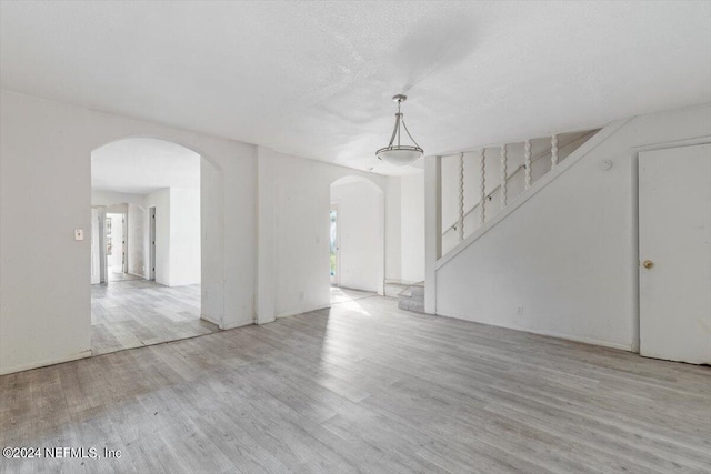 unfurnished living room with arched walkways, wood finished floors, and stairway