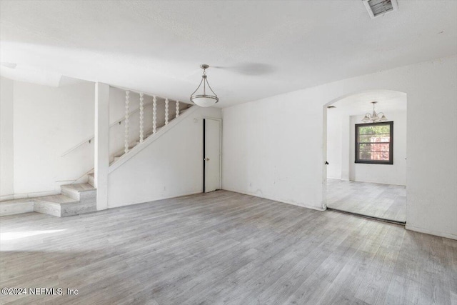 unfurnished living room featuring stairway, wood finished floors, arched walkways, a notable chandelier, and visible vents