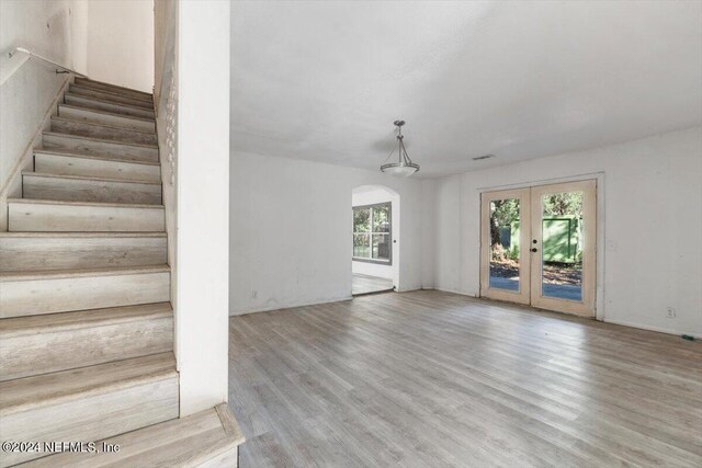 stairs with french doors, wood finished floors, and arched walkways