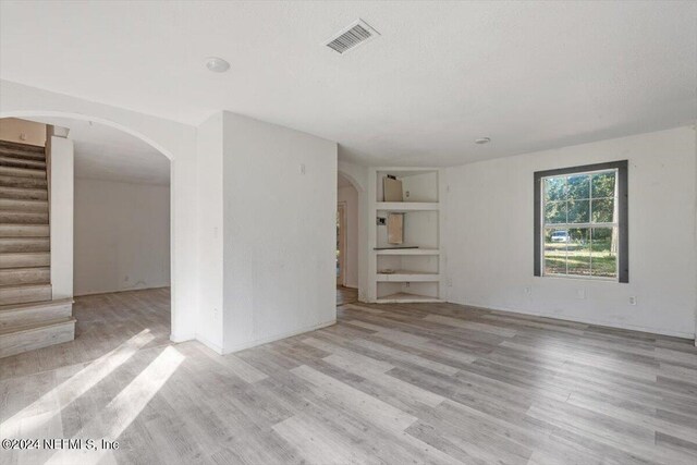 unfurnished living room with stairway, wood finished floors, built in shelves, arched walkways, and visible vents