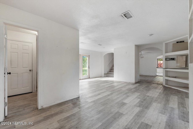 unfurnished living room with stairway, wood finished floors, visible vents, arched walkways, and a textured ceiling