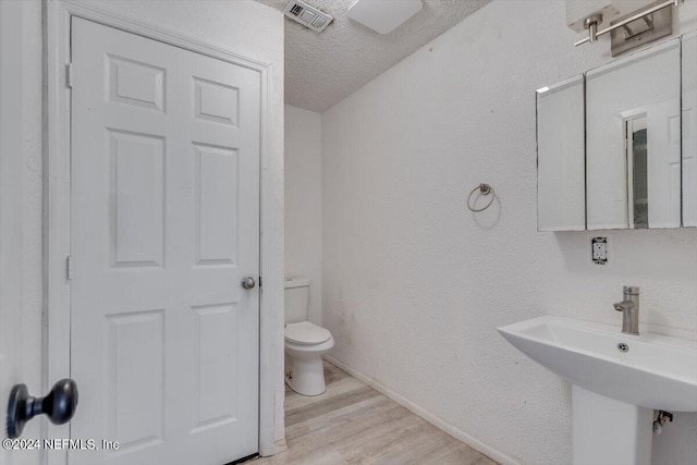 bathroom featuring toilet, wood finished floors, a textured ceiling, baseboards, and visible vents