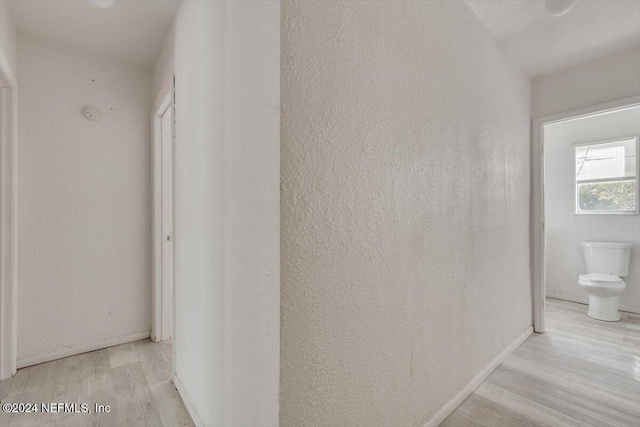hall featuring wood finished floors, baseboards, and a textured wall