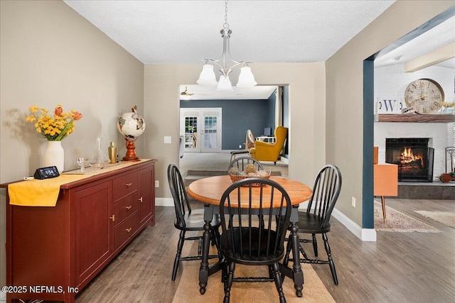 dining area with a textured ceiling, a fireplace, wood finished floors, baseboards, and a chandelier