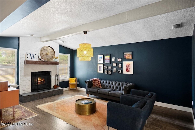 living room with a textured ceiling, visible vents, a tile fireplace, wood finished floors, and baseboards