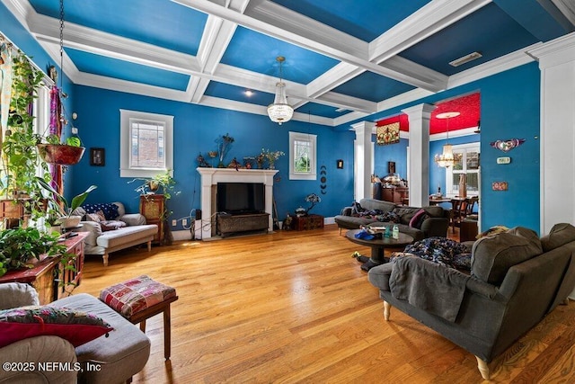 living area featuring decorative columns, wood finished floors, a wealth of natural light, and an inviting chandelier