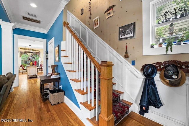 staircase featuring wood finished floors, ornamental molding, and decorative columns