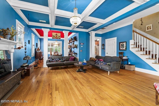 living area with ornate columns, wood finished floors, stairs, and crown molding