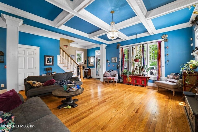 living area with decorative columns, wood finished floors, coffered ceiling, and stairs