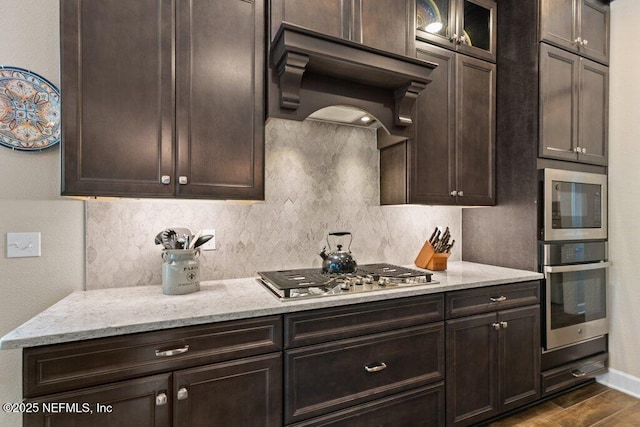 kitchen with custom exhaust hood, dark wood-type flooring, tasteful backsplash, light stone counters, and appliances with stainless steel finishes