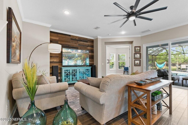 living area featuring visible vents, wood walls, ceiling fan, and crown molding