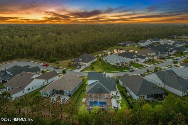 aerial view at dusk featuring a residential view and a forest view