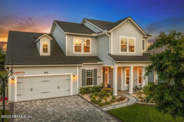 view of front of property featuring a porch, decorative driveway, a shingled roof, and a garage