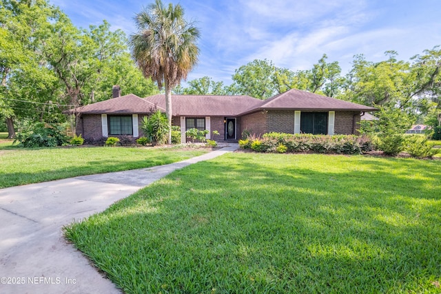 ranch-style home with a chimney, a front yard, and brick siding