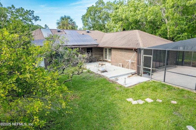 rear view of property featuring a patio area, a shingled roof, solar panels, a lawn, and brick siding