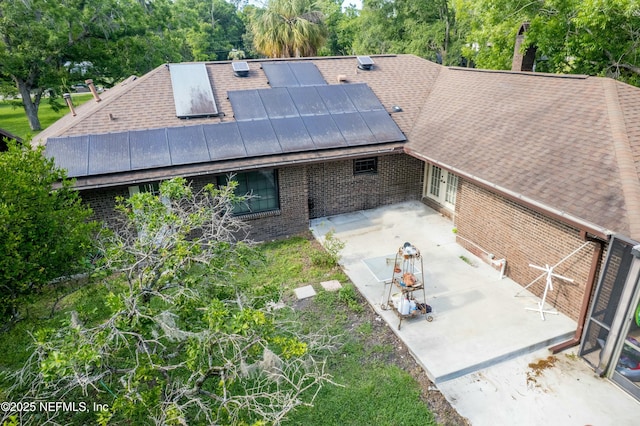 back of house featuring a patio, brick siding, a chimney, roof with shingles, and roof mounted solar panels